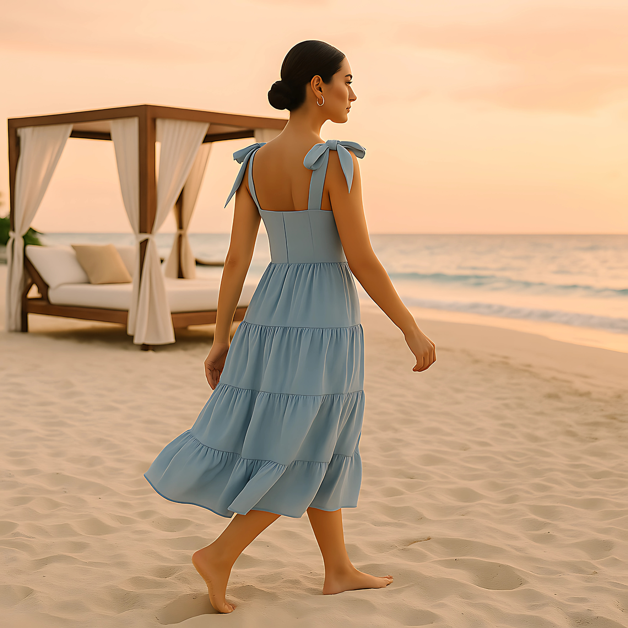 Woman wearing Clio Tiered Midi Dress with bow-tied straps and square neckline, walking on beach at sunset in soft powder blue.