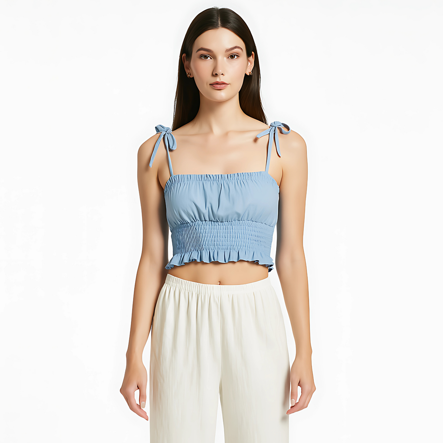 Woman wearing sky blue ruched cami top with tie straps, smocked waist, and ruffle hem; styled with white pants.
