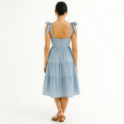 Back view of Clio Tiered Midi Dress in soft powder blue with bow-tied shoulder straps and tiered skirt, ideal for bridal or resortwear.