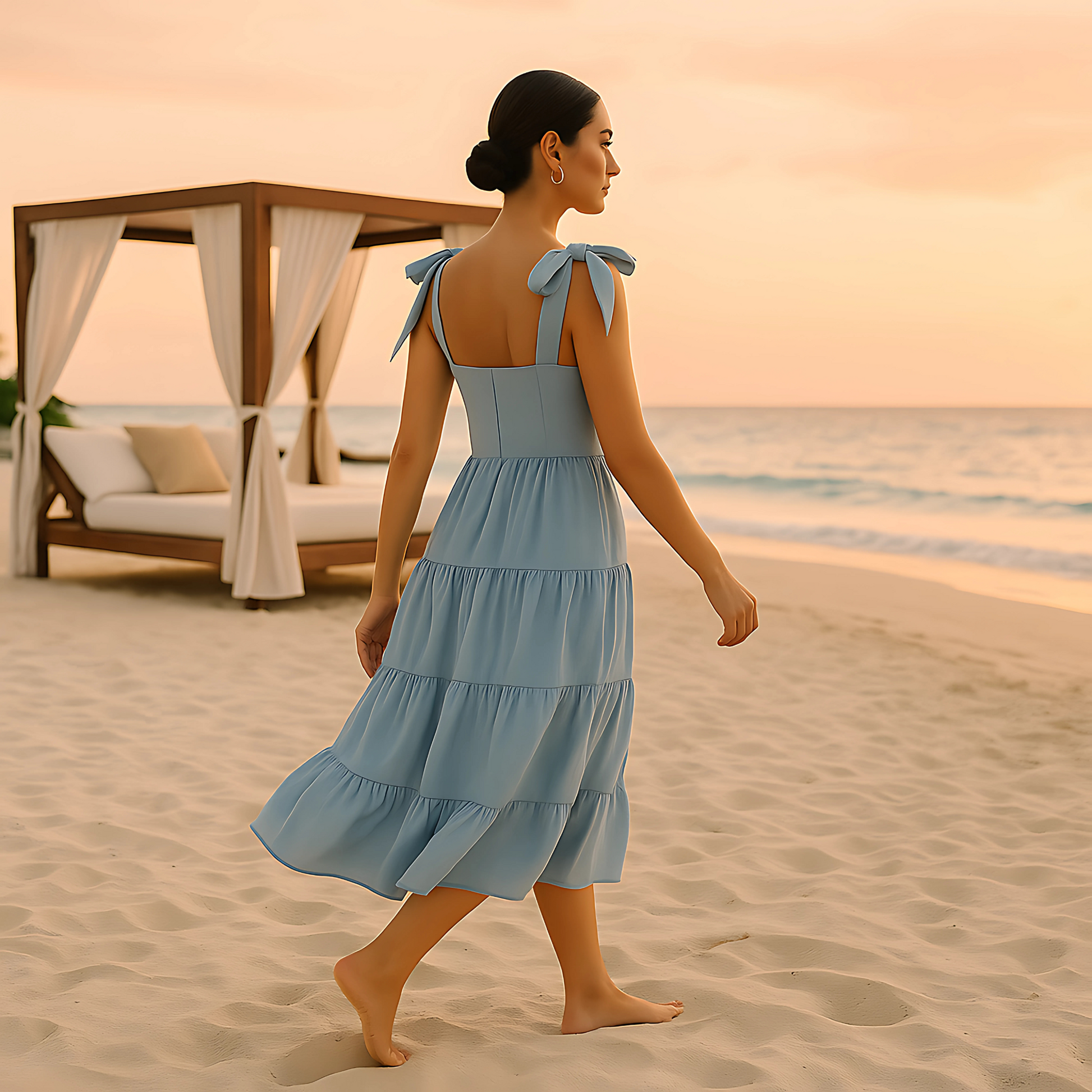Woman wearing Clio Tiered Midi Dress with bow-tied straps and square neckline, walking on beach at sunset in soft powder blue.