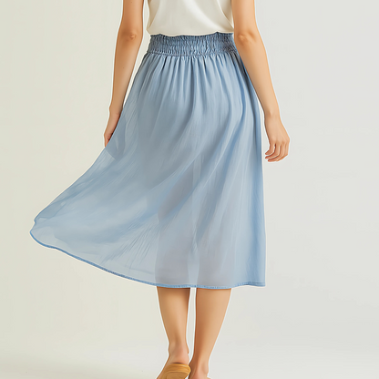 Woman wearing Isla Elastic Midi Skirt in Cloud Blue, featuring a wide elastic waistband and flowing fabric for resort and travel wear.