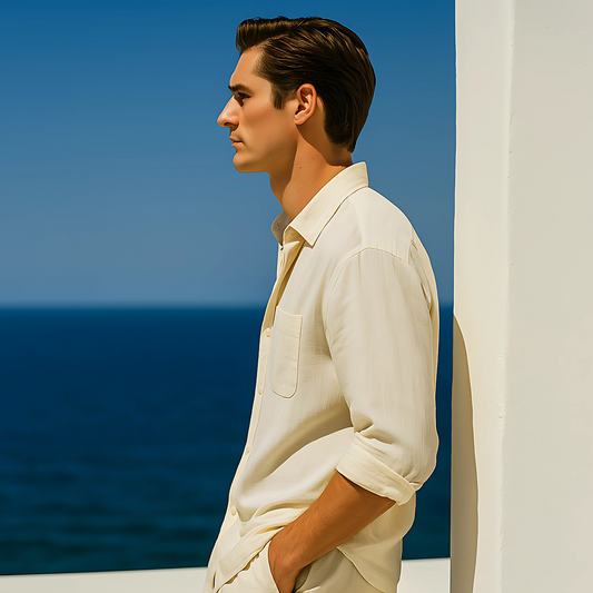 Man wearing a white Solstice Linen Shirt & Short Set, standing by a white wall overlooking the ocean.
