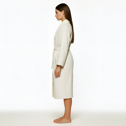 Woman wearing The Aedon Spa Robe in Ecru/Cream with shawl collar and belt, ideal for spa and resort use.