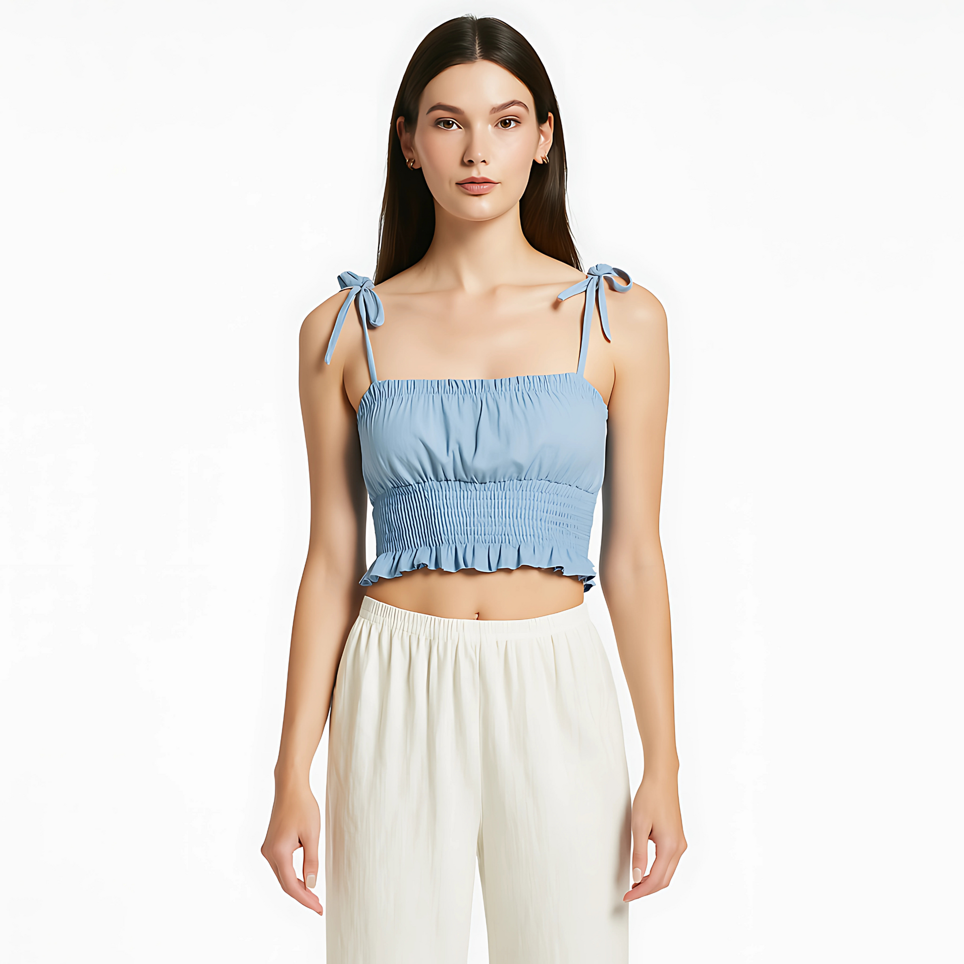 Woman wearing sky blue ruched cami top with tie straps, smocked waist, and ruffle hem; styled with white pants.