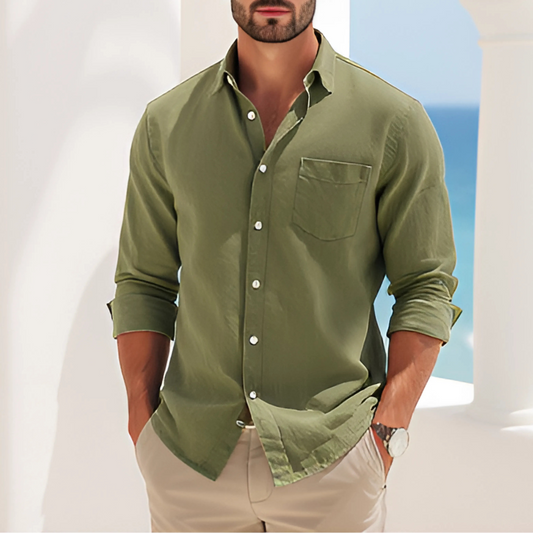 Man wearing a Verde Coastline Shirt, standing against a coastal background with ocean view. Casual and elegant style in green.